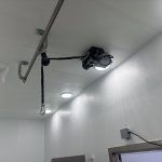 Ceiling-mounted device with cables in a white hallway near a doorway.