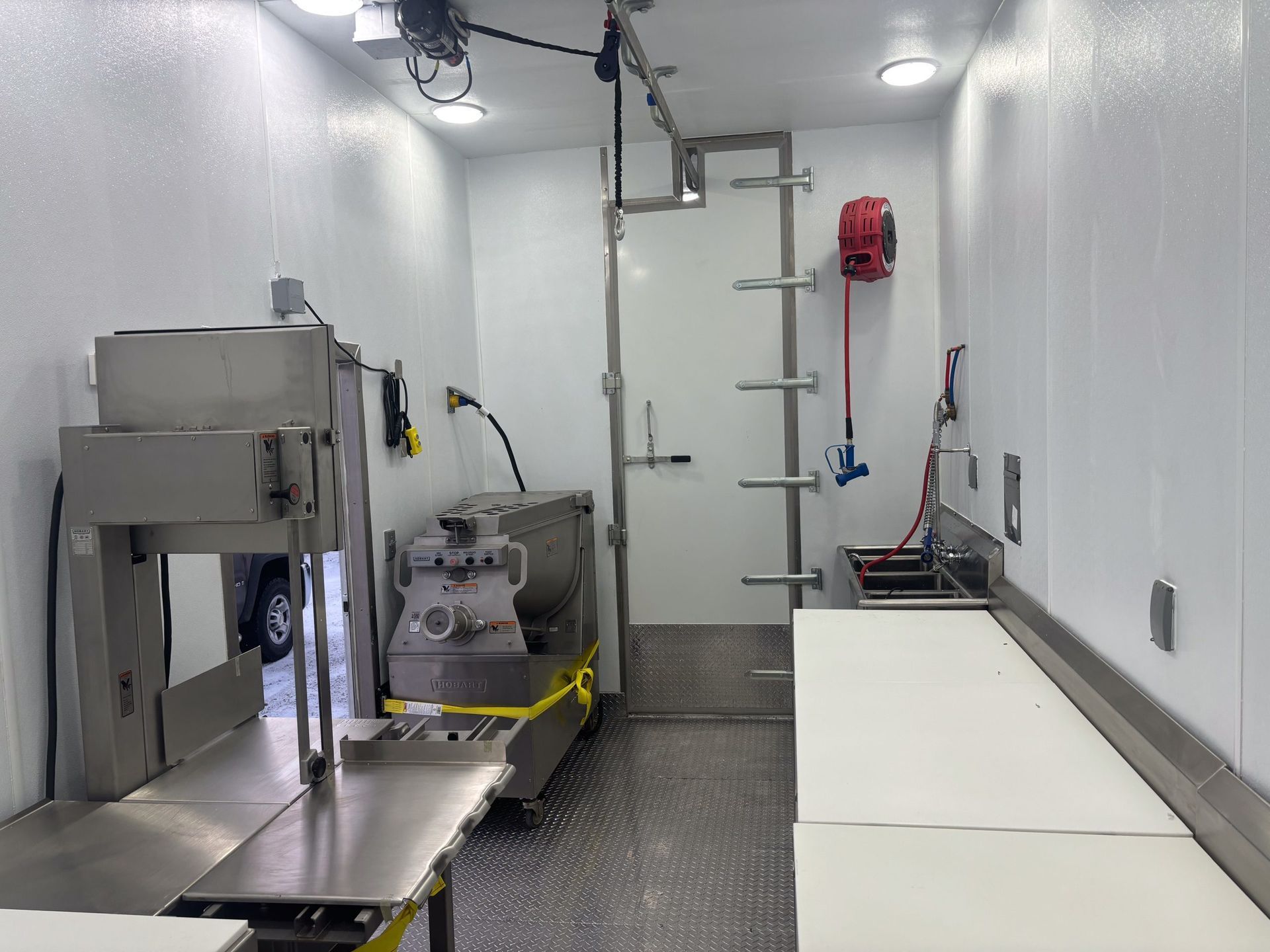 Small industrial room with stainless equipment, a utility cart, and white tables along the right wall.