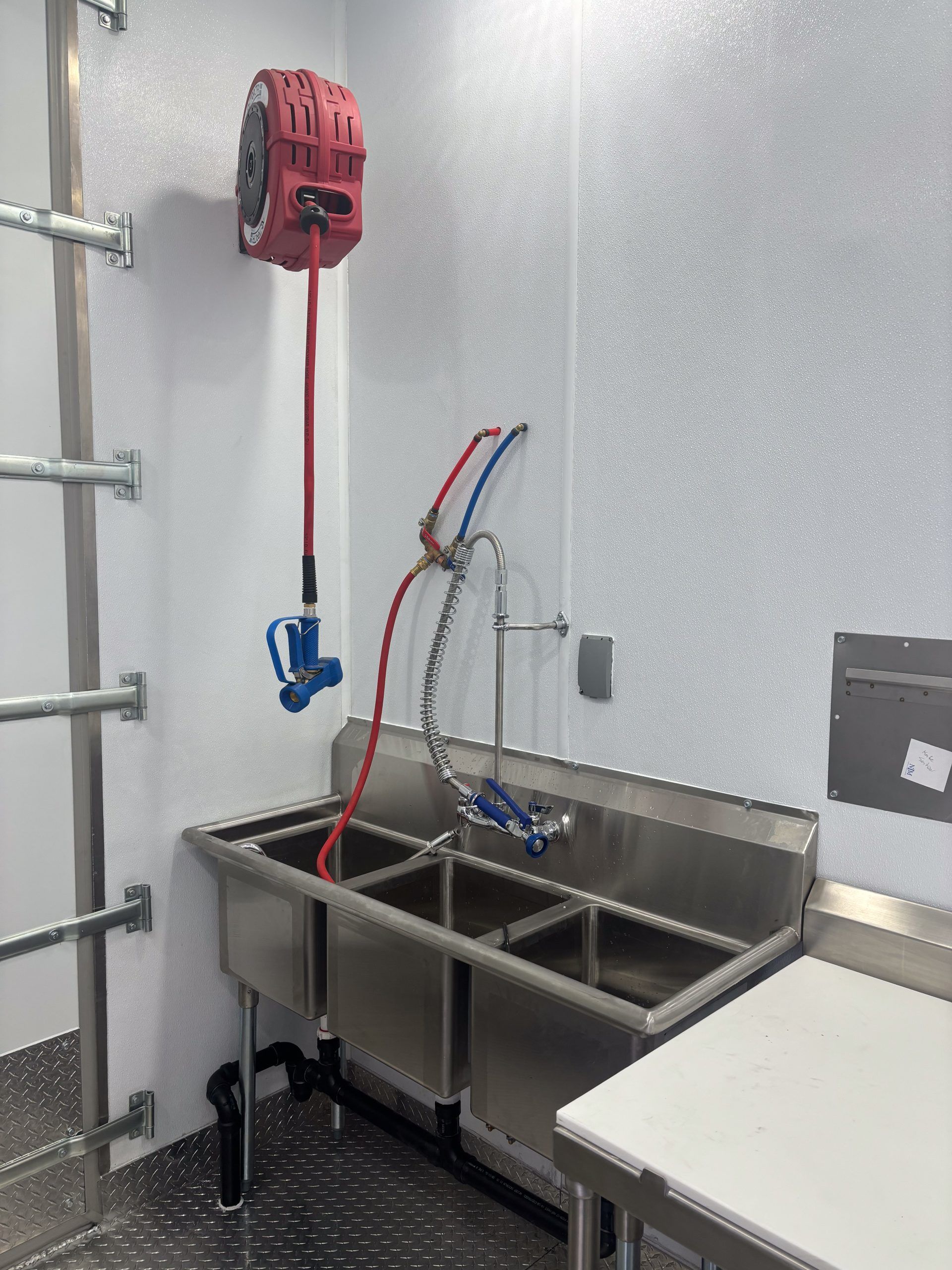 Stainless steel utility sink with red hose reel and faucet in a clean industrial room
