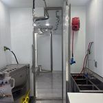 Commercial kitchen with stainless-steel equipment, sink, and wall-mounted fire extinguisher.
