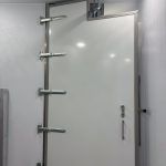 White metal door with a silver handle and horizontal hinges in an industrial interior.