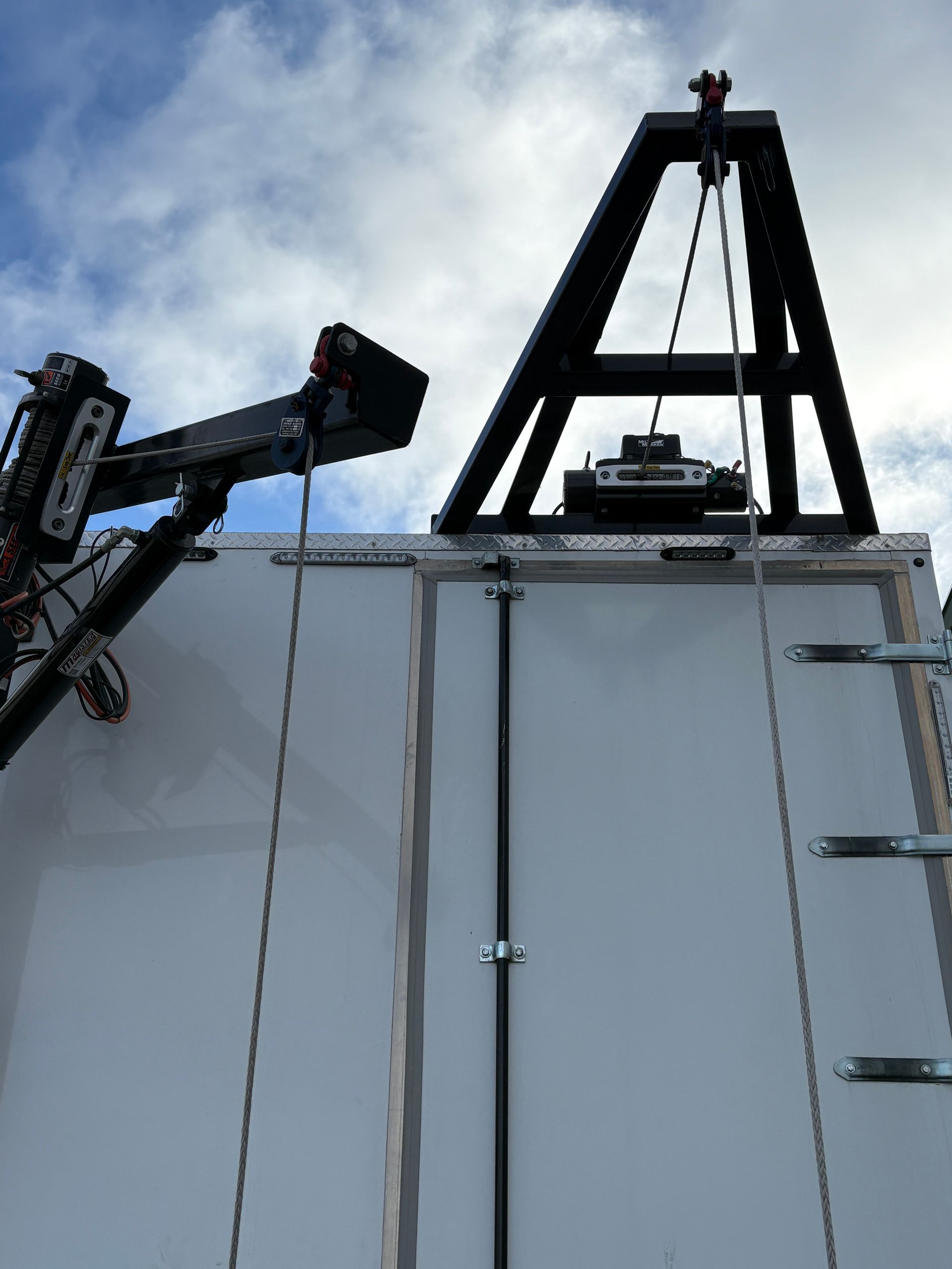 Crane lifting a large white container beneath a cloudy sky, with a metal ladder on the side.