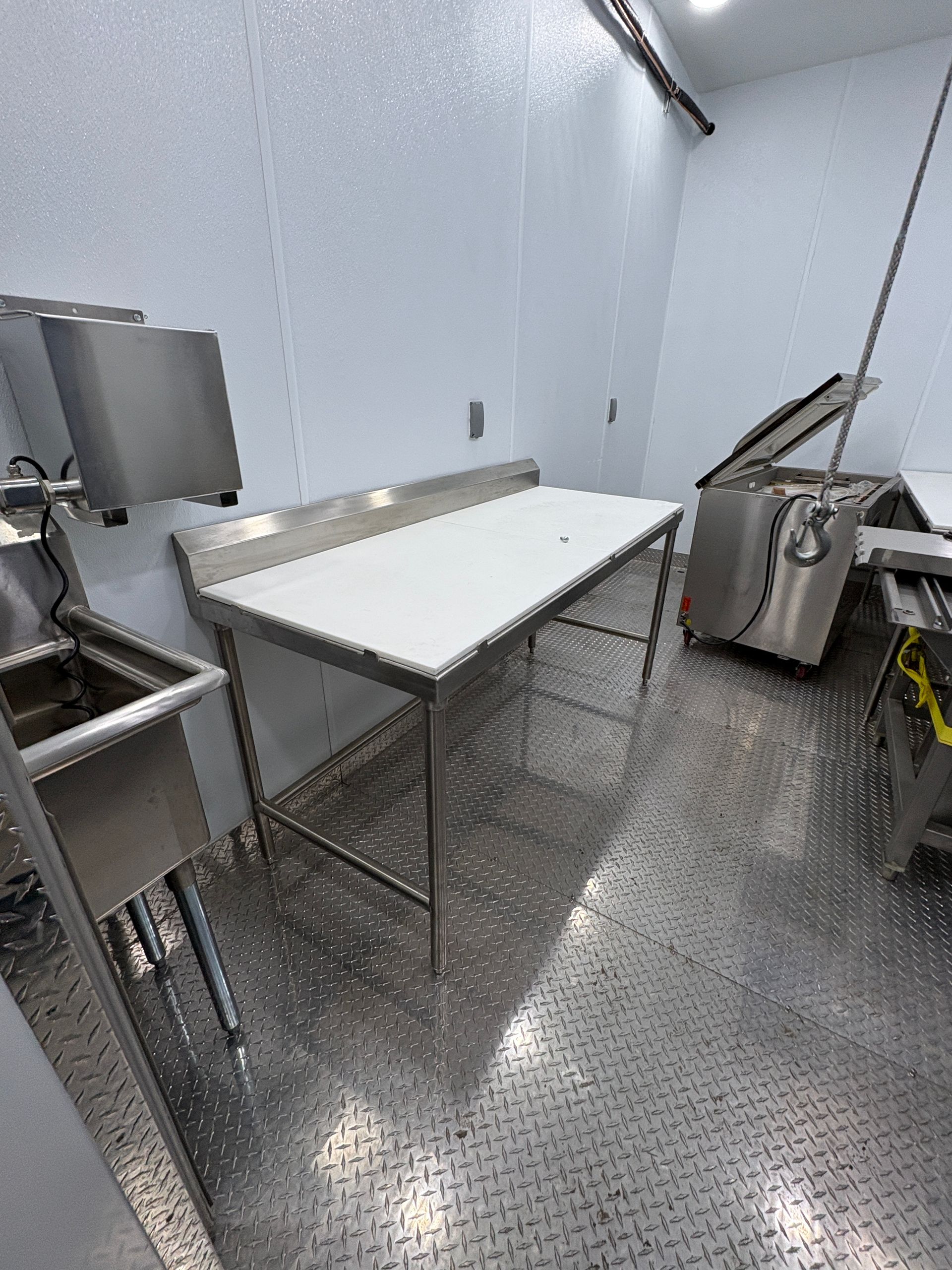 Stainless steel prep table in a commercial kitchen with metal sink, equipment, and tiled floor