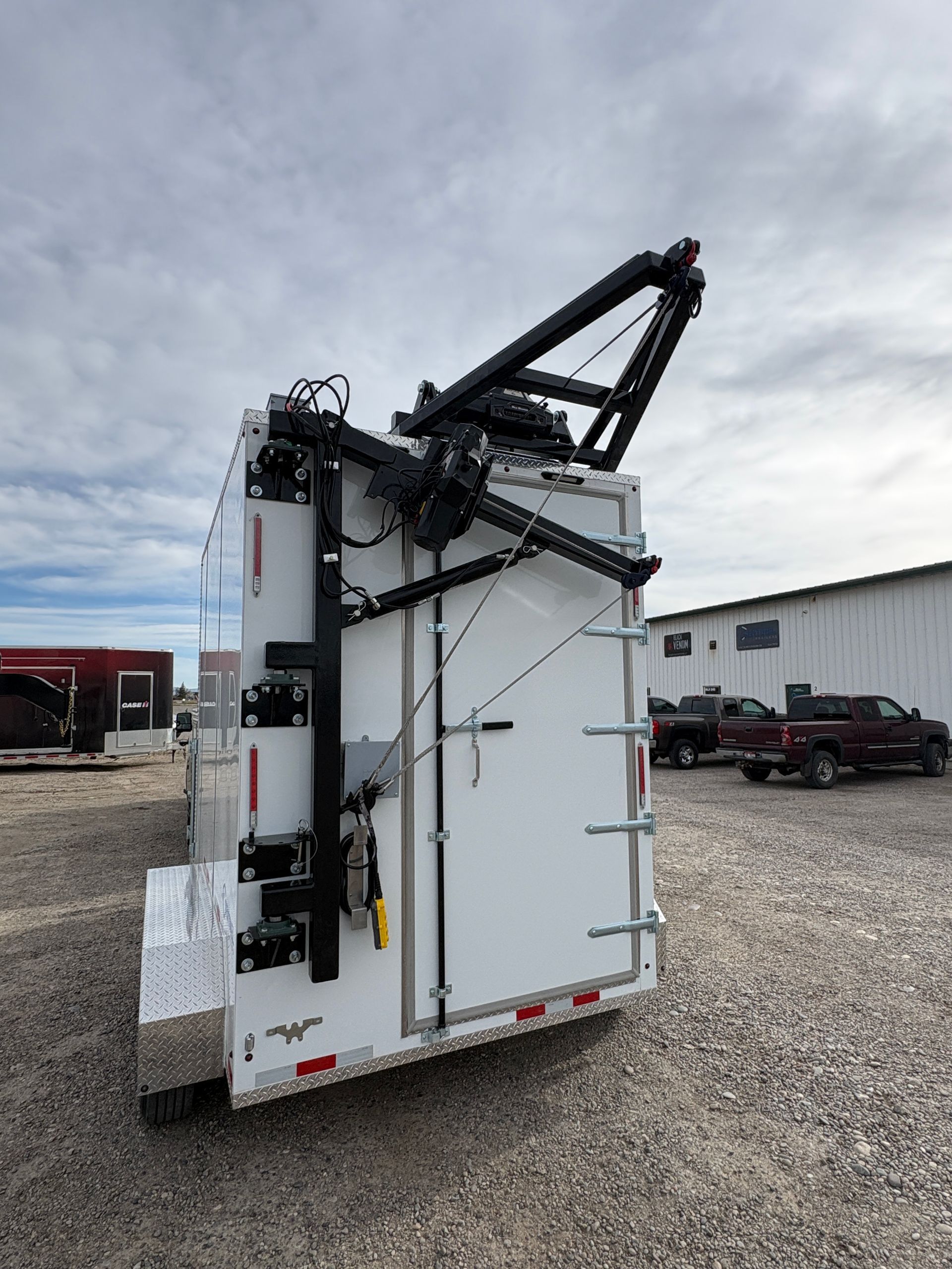White utility truck with folded crane arm parked on gravel under a cloudy sky