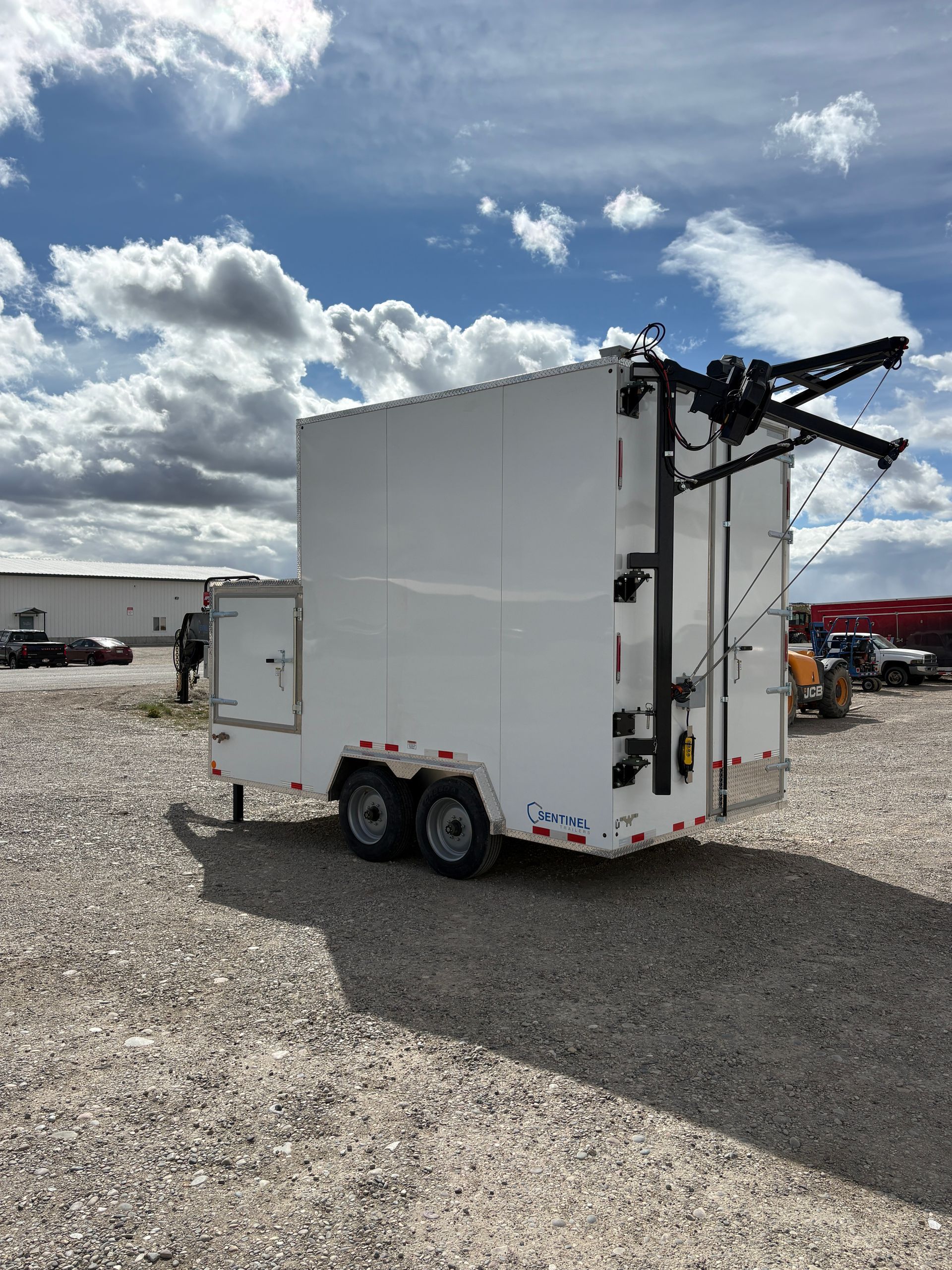 White mobile trailer with rooftop equipment parked on gravel under a cloudy sky