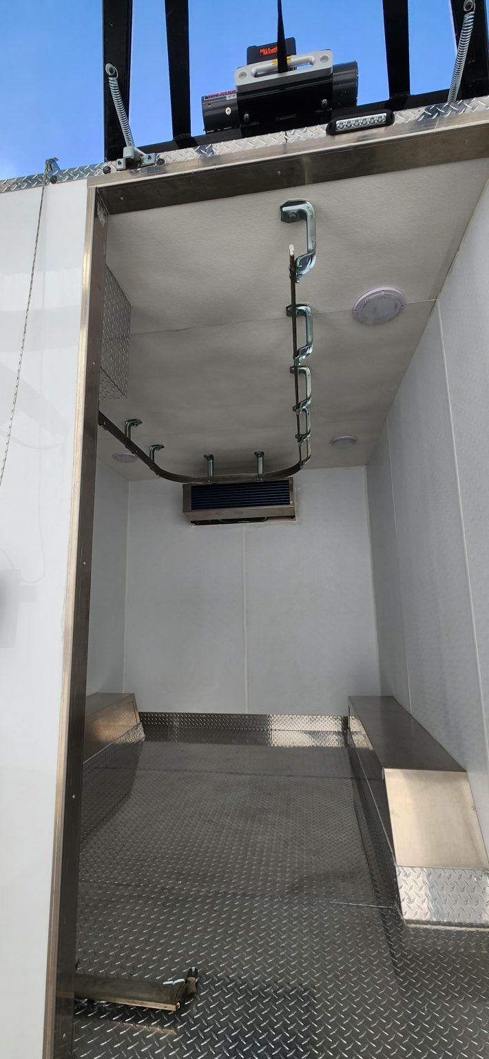 Empty white utility compartment with a diamond-plate floor and a rail for moving carcasses in mobile butcher trailer