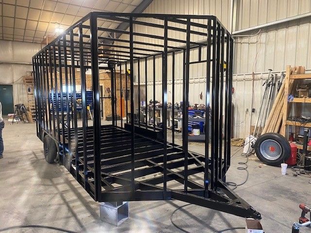 Black metal butcher trailer frame in a workshop, with open sides and a ramp, under construction.