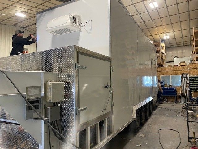 Mobile slaughter trailer for butchers in a warehouse, with a worker standing on top beside a ladder.