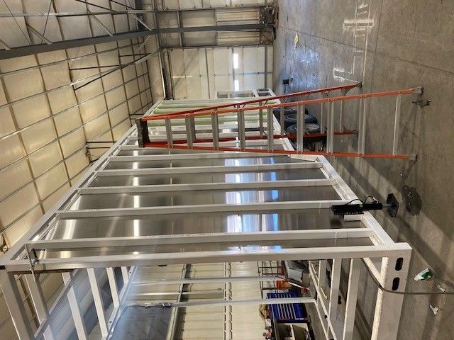 Warehouse interior with metal framing, red rails, and ladders along a concrete floor