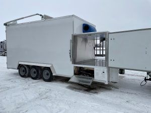 White mobile Sentinel trailer with three axles and an open side gut compartment in a snowy outdoor setting