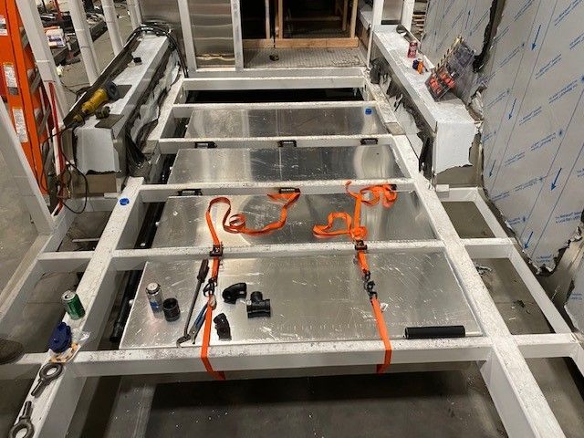 Construction site with white metal framing, orange straps, and tools on the floor in a narrow room
