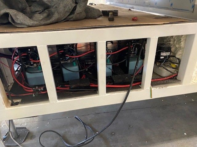 Open cubby cabinet with exposed wiring and electronics inside, under a workbench in a workshop, a view beneath a Sentinel Trailer