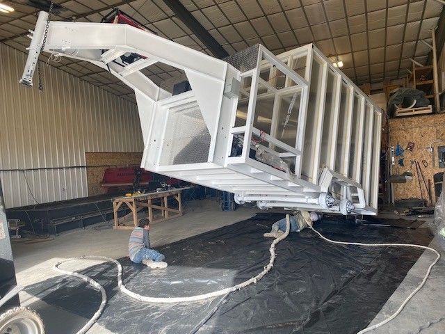 Large white industrial machine being repaired inside a warehouse, with a person crouched beneath it. Sentinel trailers behind the scenes