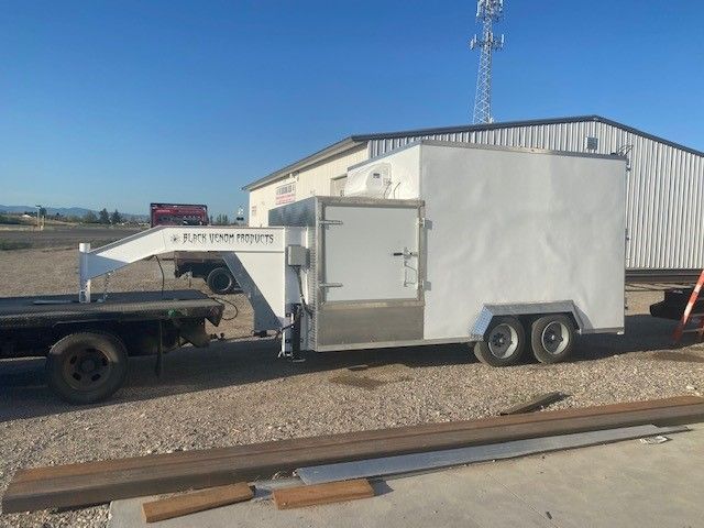 White equipment trailer attached to a truck on a gravel lot beside a metal building