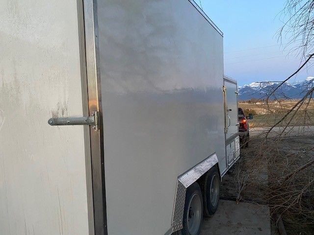 White butcher enclosed trailer with side door, parked on a dirt path near mountains at dusk