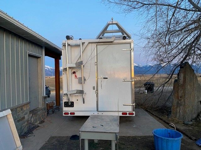 Mobile meat processing unit parked between buildings at dusk, with a blue bucket and concrete path nearby.