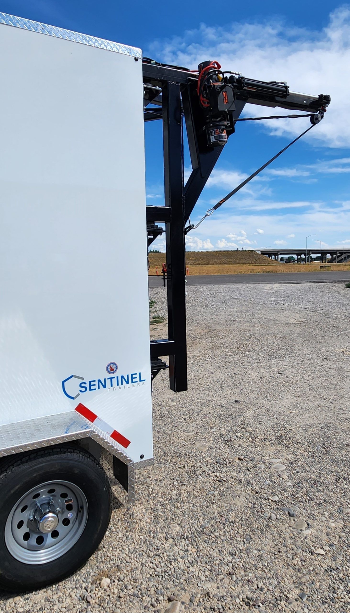 White Sentinel trailer with a black crane arm parked on gravel under a blue sky.