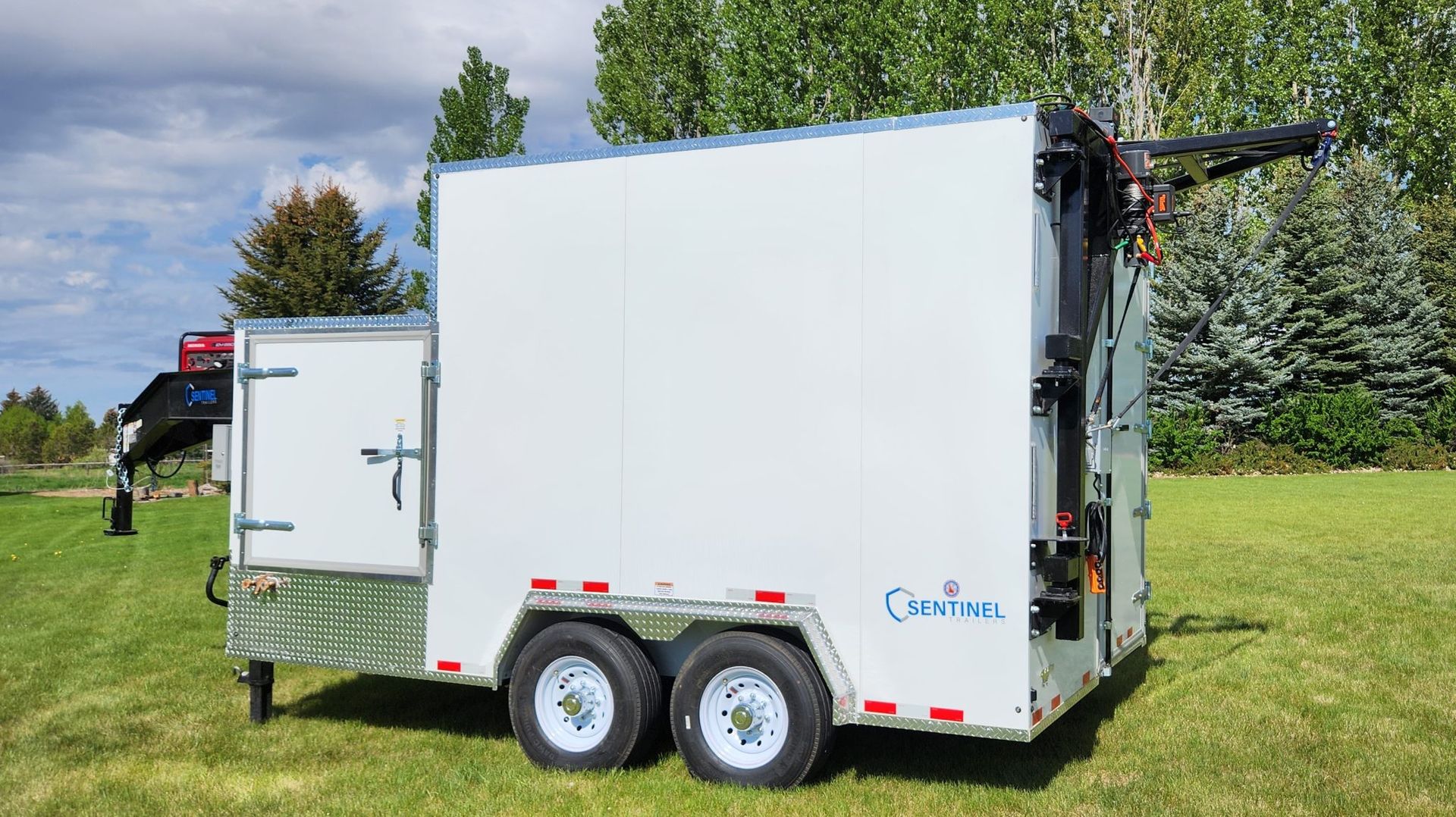 White trailer-mounted machine on grass, with twin axles and a rear hatch, under a cloudy sky.