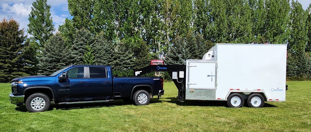 Black pickup truck towing a white cargo trailer on grass with trees in the background