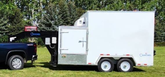 Pickup towing a white enclosed mobile butcher trailer on grass beside trees