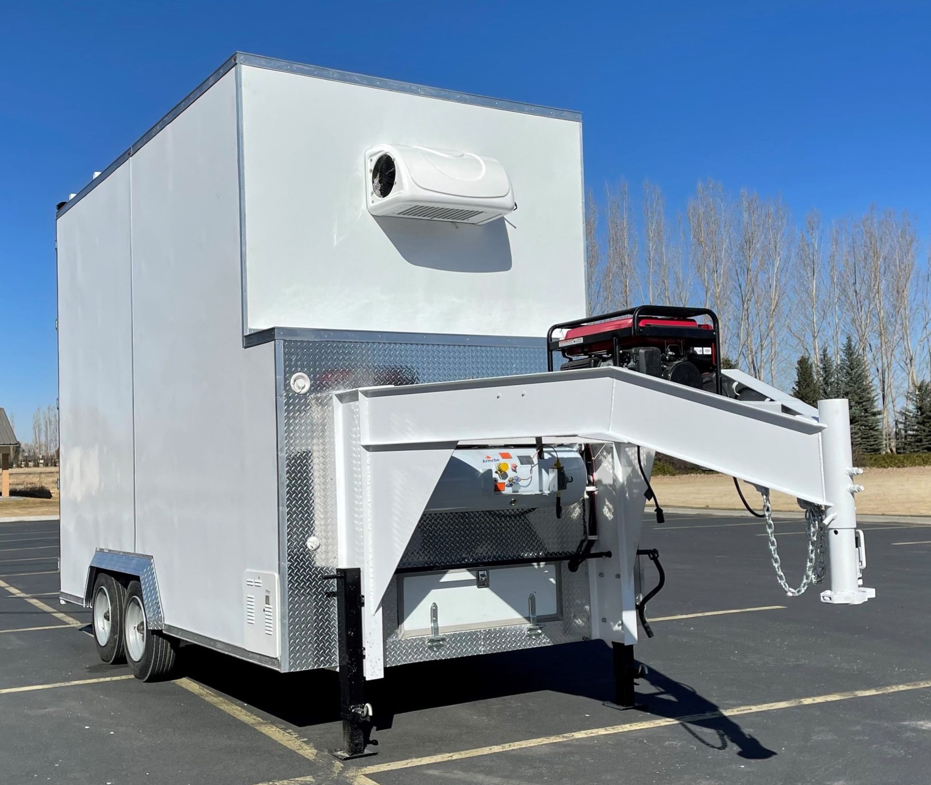 White enclosed trailer with a front cargo ramp and rooftop unit, parked outdoors on pavement under a clear sky