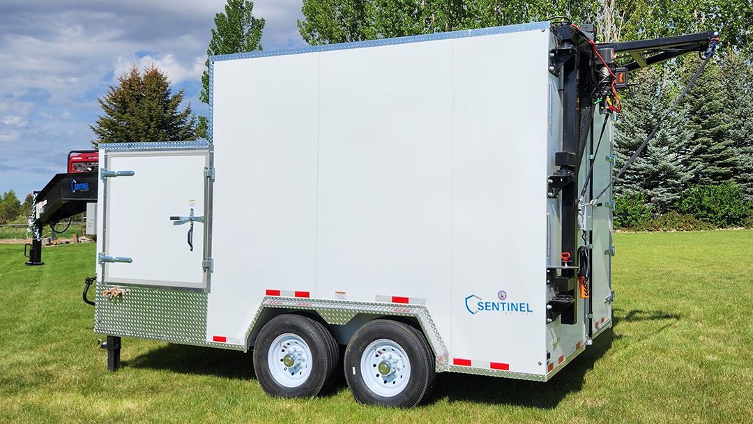 White enclosed utility trailer for meat processing with two axles parked on grass in a sunny outdoor setting