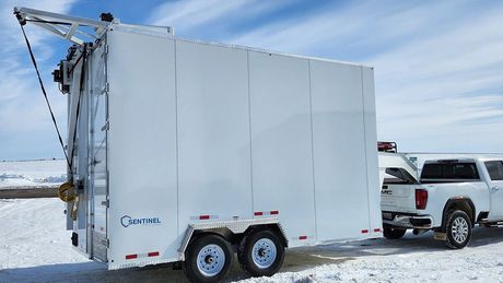 White enclosed refrigerated trailer for meat processing parked in snowy landscape beside a white pickup truck
