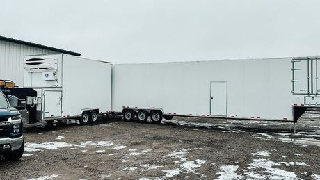 White refrigerated butcher trailer parked in a snowy lot, side door open, with a truck beside it