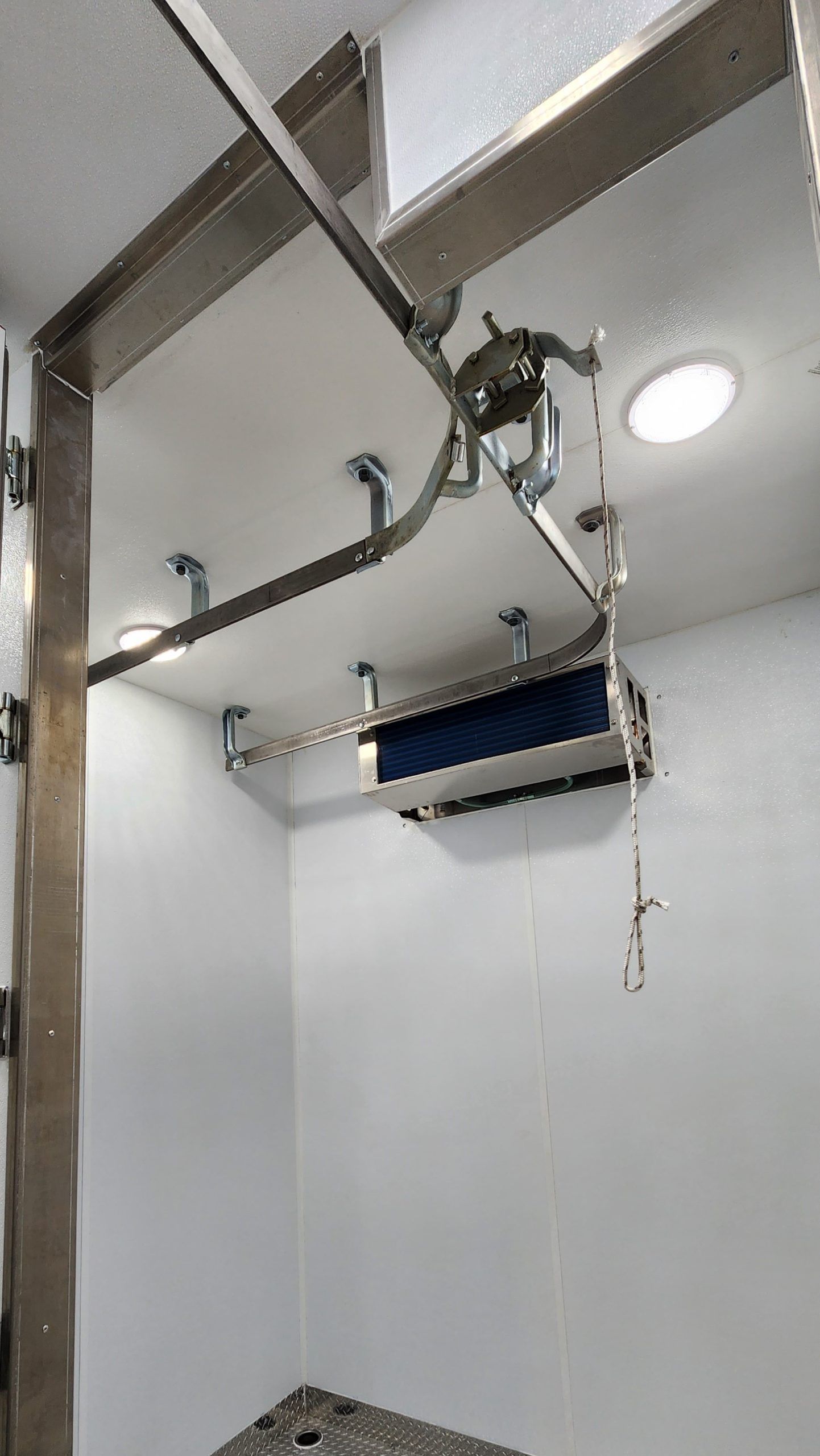 Ceiling-mounted carcass lift track with blue sling over a bed area, near a round ceiling light