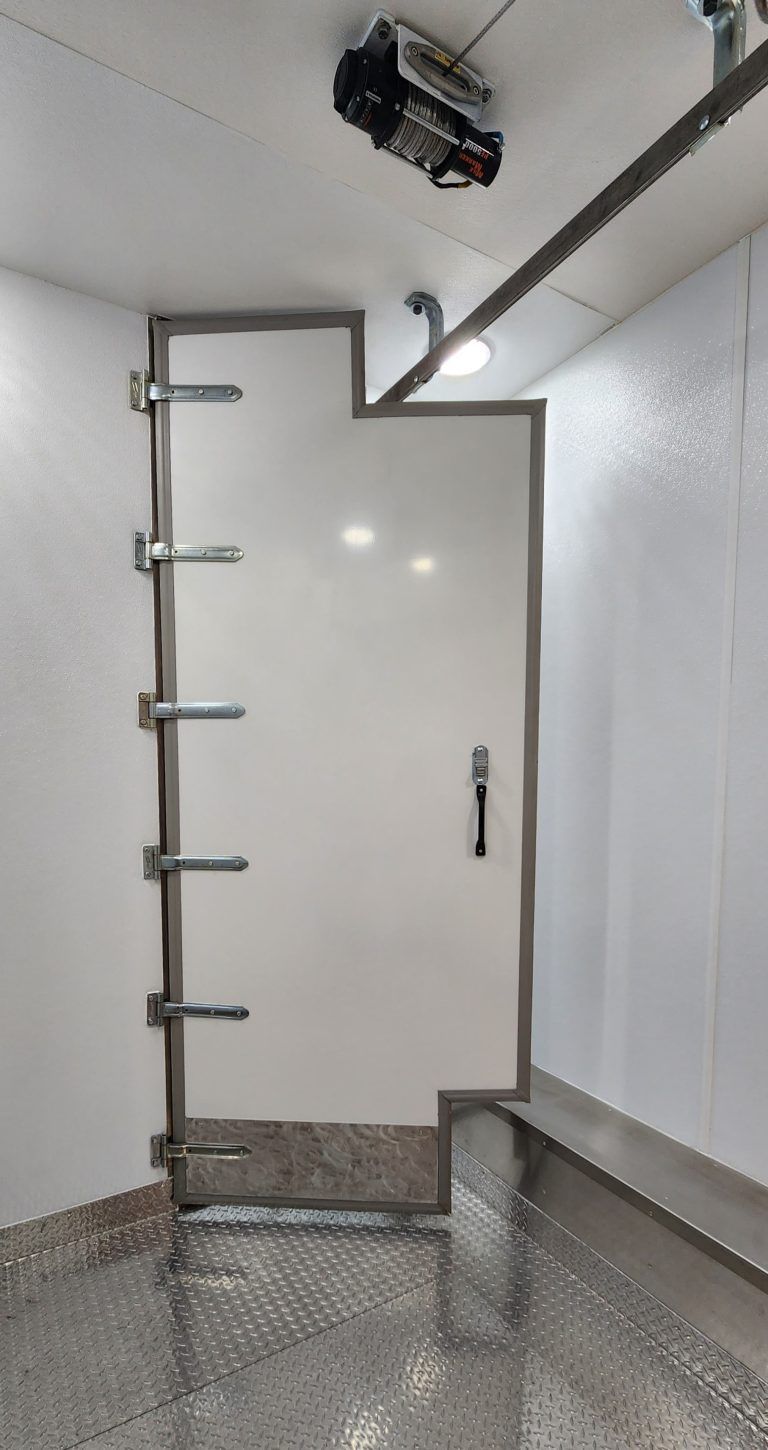 Industrial freezer room with a white walk-in door, metal ladder, and overhead hardware in refrigerated trailer