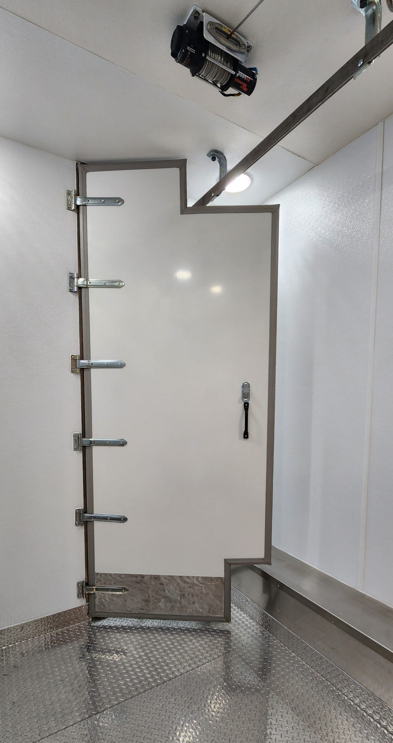 White stall door with metal latch and hanging bar inside a mobile meat processing unit made by Sentinel Trailers