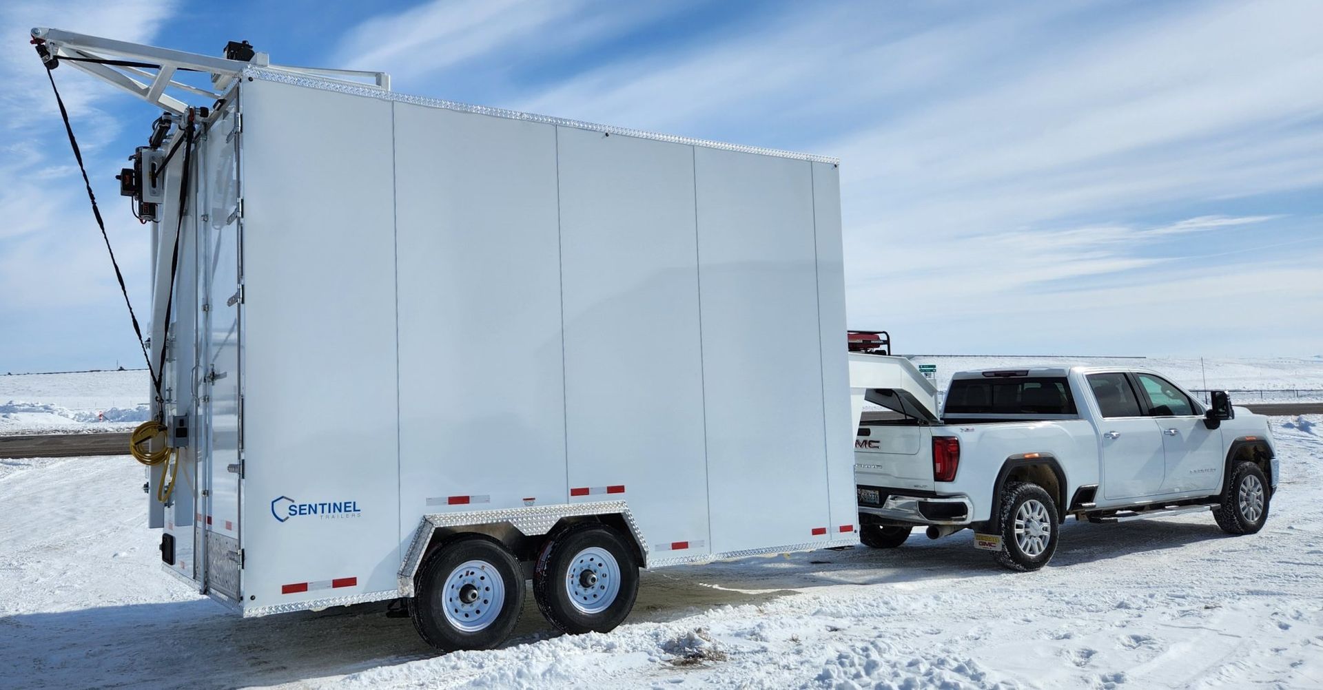 White pickup truck towing a large white enclosed butcher trailer across a snowy landscape under a blue sky
