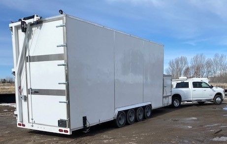 White butcher trailer hitched to a white pickup truck on a muddy lot under a blue sky
