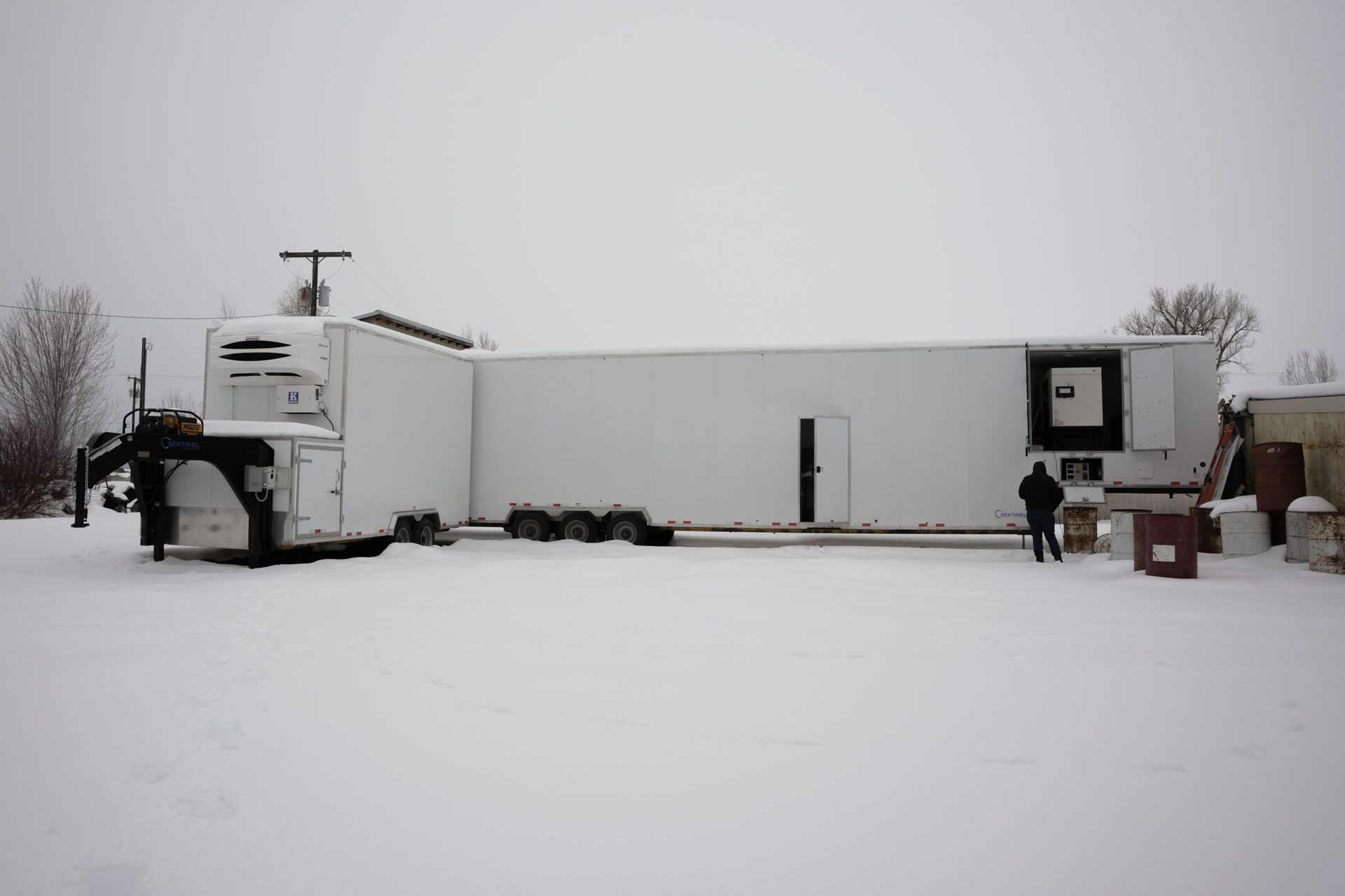 Snow-covered USDA certified meat processing trailer with a person near the entrance and utility equipment outside