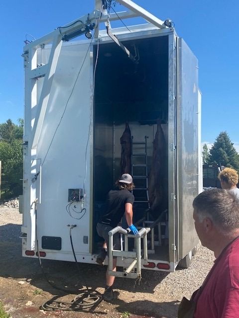 Two people unload equipment from the back of a white Sentinel trailer outdoors.