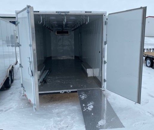 Open white  meat processing trailer with ramp lowered onto snowy ground, empty inside.