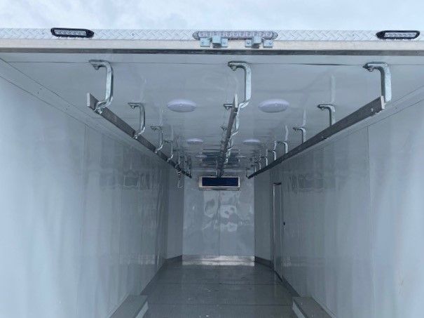 Inside of a clean white refrigerated trailer with overhead rails and hanging hooks
