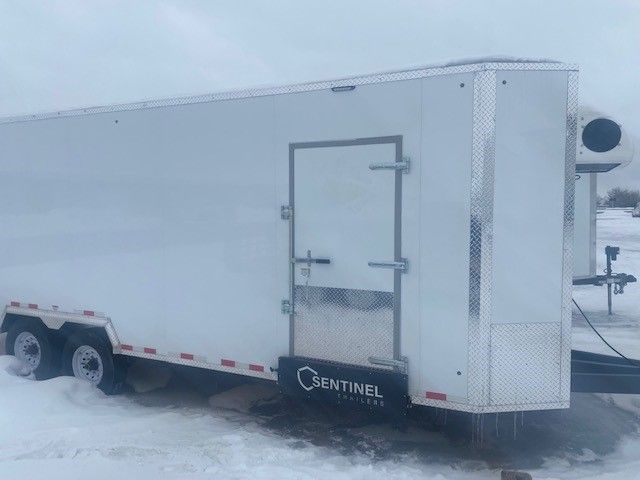 White enclosed trailer for meat processing on snowy ground with a side door and dual axles