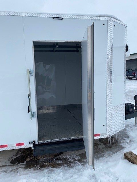 Open white cargo trailer for meat processing with side door ajar in a snowy lot
