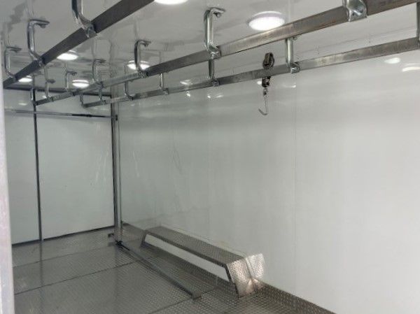 Inside view of a meat processing trailer with white walls, metal rails overhead, and a long bench along the side.