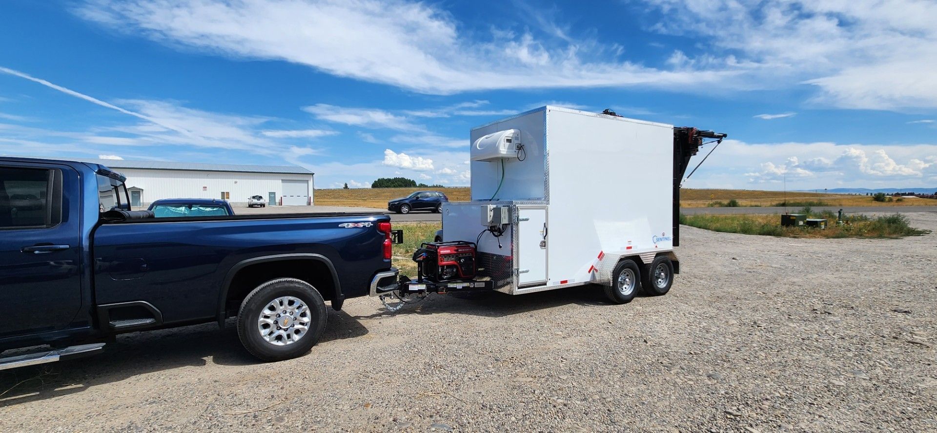 Black pickup truck towing a white enclosed Sentinel butcher trailer on a gravel lot under a blue sky