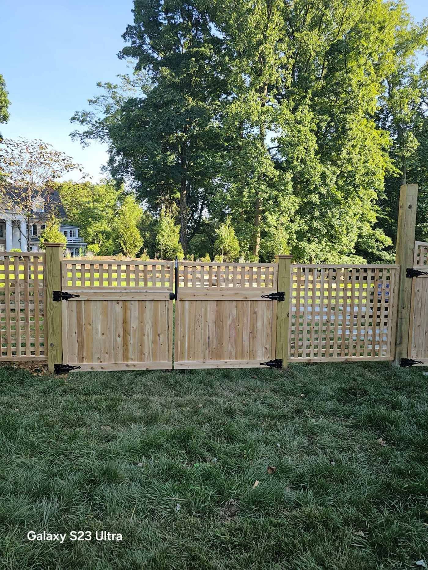 A man is standing in front of a wooden fence in a backyard.