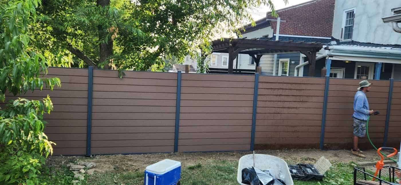 A man is standing in front of a wooden fence in a backyard.