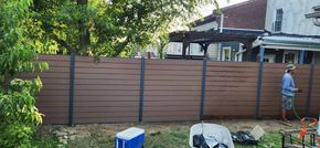A man is standing in front of a wooden fence in a backyard.