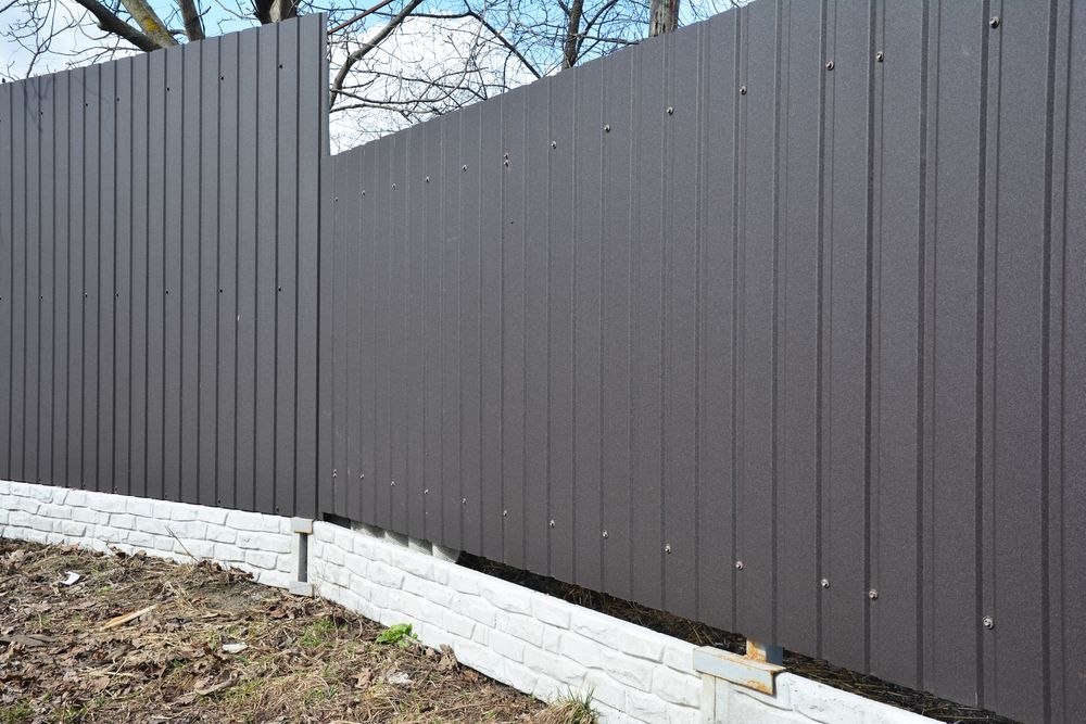 A man is standing in front of a wooden fence in a backyard.