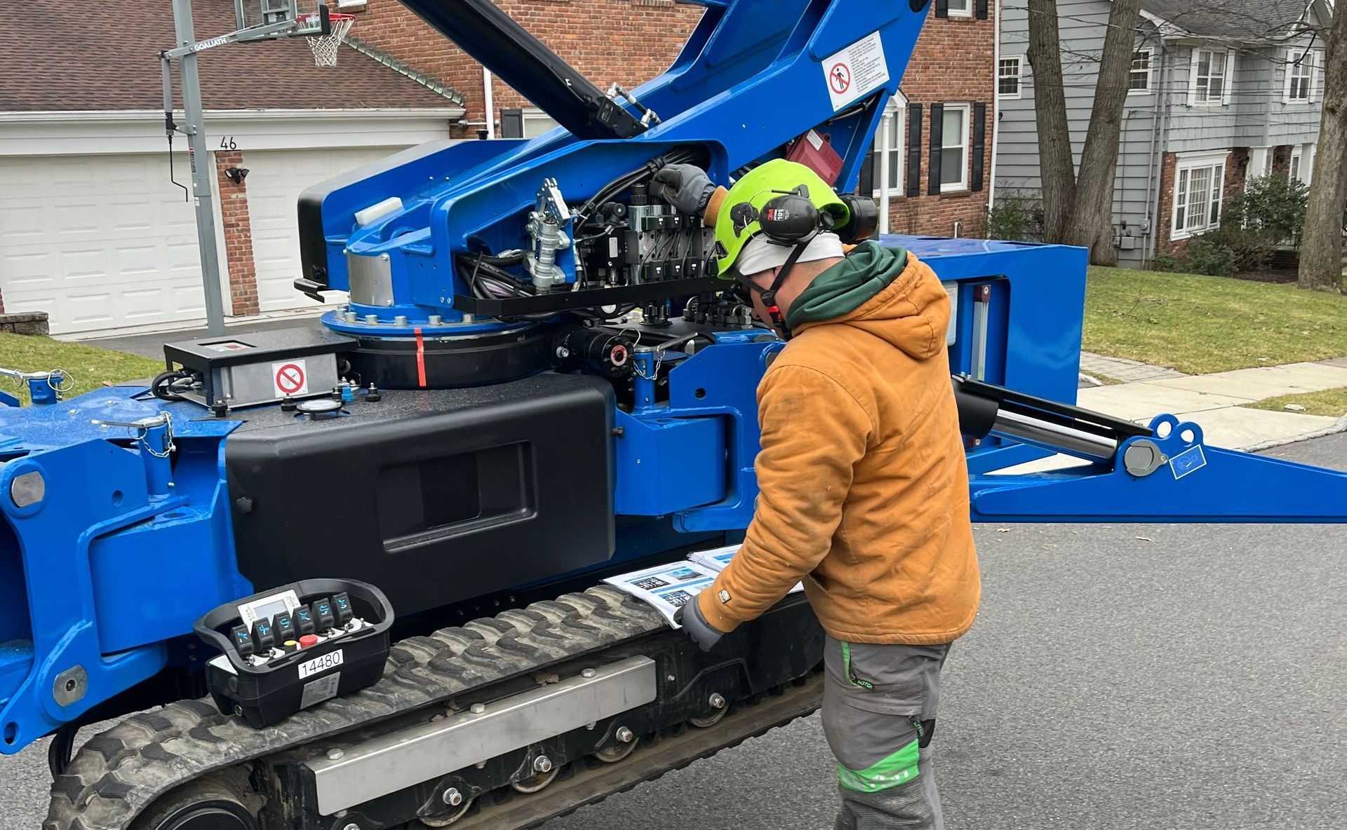 Person in safety gear inspecting a blue tracked lift, parked on a street.