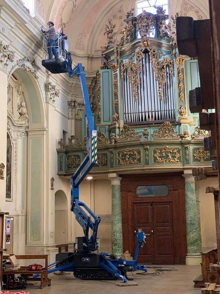 A person in a lift working on the decorative pipe organ in a church.