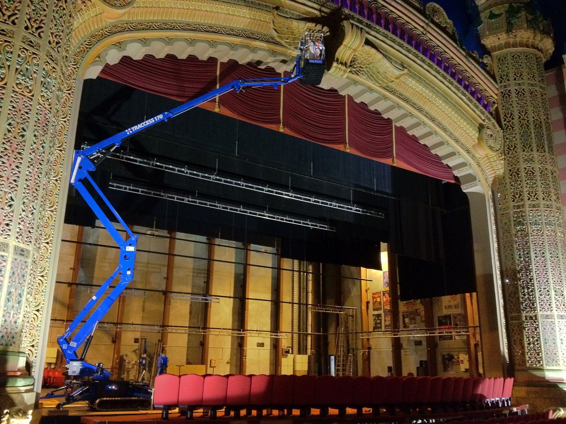 Blue lift inside a theater stage, near decorative ceiling, with stage curtains and red seats.