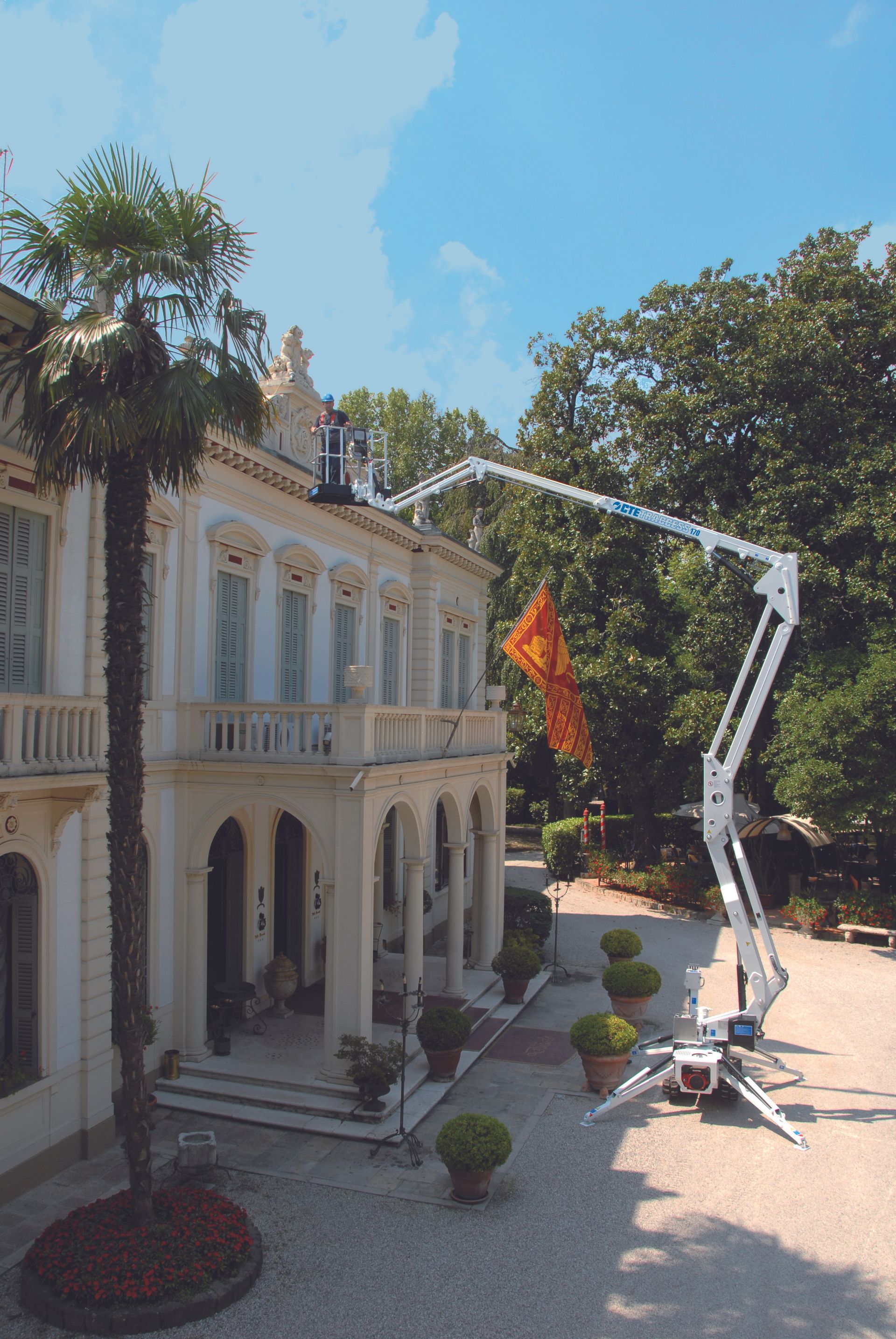 White lift truck with extended arm reaching a building's roof; bright orange cloth hangs from it. 