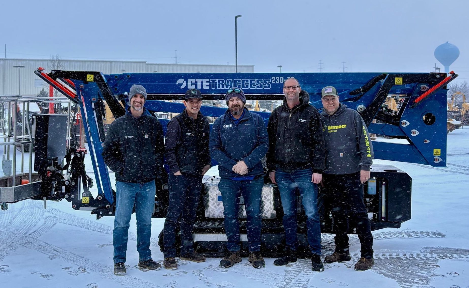 Five people pose in front of a blue CTE truck lift in a snowy outdoor setting.